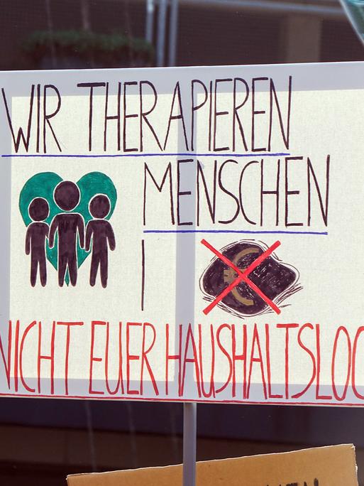 Ein Transparent mit der Aufschrift: "Wir therapien Menschen, nicht euer Haushaltsloch" auf einer Demonstration gegen Honorarkürzungen in der Psychotherapie am 19. März 2026 in Düsseldorf.