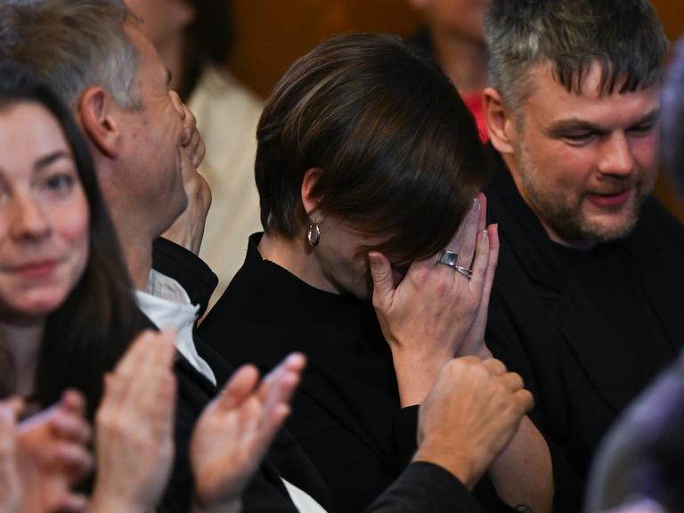 Die Schweizer Autorin Dorothee Elmiger (M, «Die Holländerinnen») reagiert bei der Bekanntgabe der Gewinnerin des Deutschen Buchpreis 2025 emotional, indem sie ihre Hände vor ihr Gesicht legt. Die Menschen um sie herum klatschen.