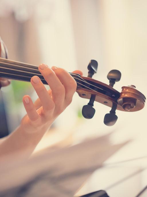Eine junge Frau spielt Violine. Das Foto zeigt ihren linken Arm und linke Hand, die die Geige halten