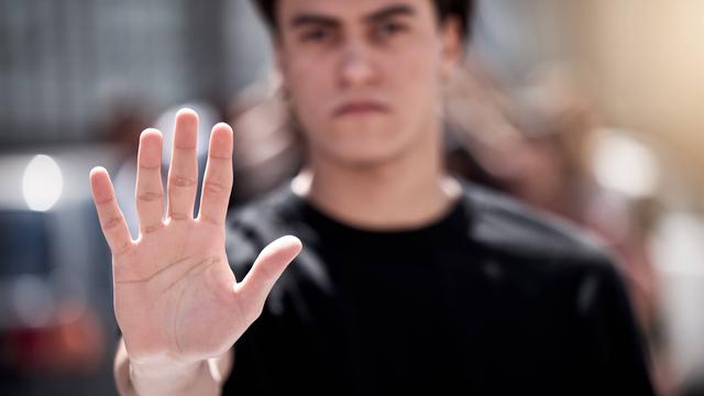 Eine ausgestreckte Hand, die Stop signalisiert, der Mann im Hintergrund ist unscharf