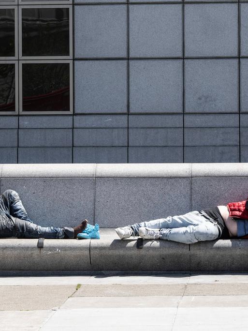 Zwei obdachlose Männer schlafen in San Franzisko auf einer Beton-Bank.