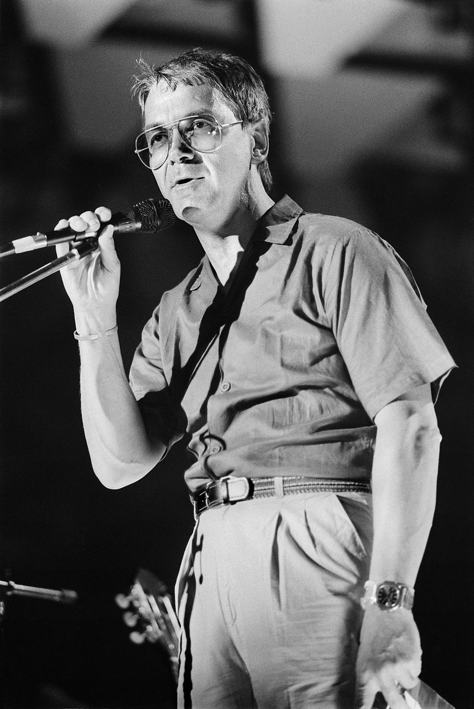 Claude Nobs 1985. Ein Mann steht auf einer Bühne und spricht in ein Mikrofon.