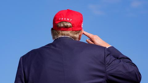 Donald Trump ist von hinten zu sehen, er trägt ein rotes Basecap mit der Aufschrift "Trump" 
