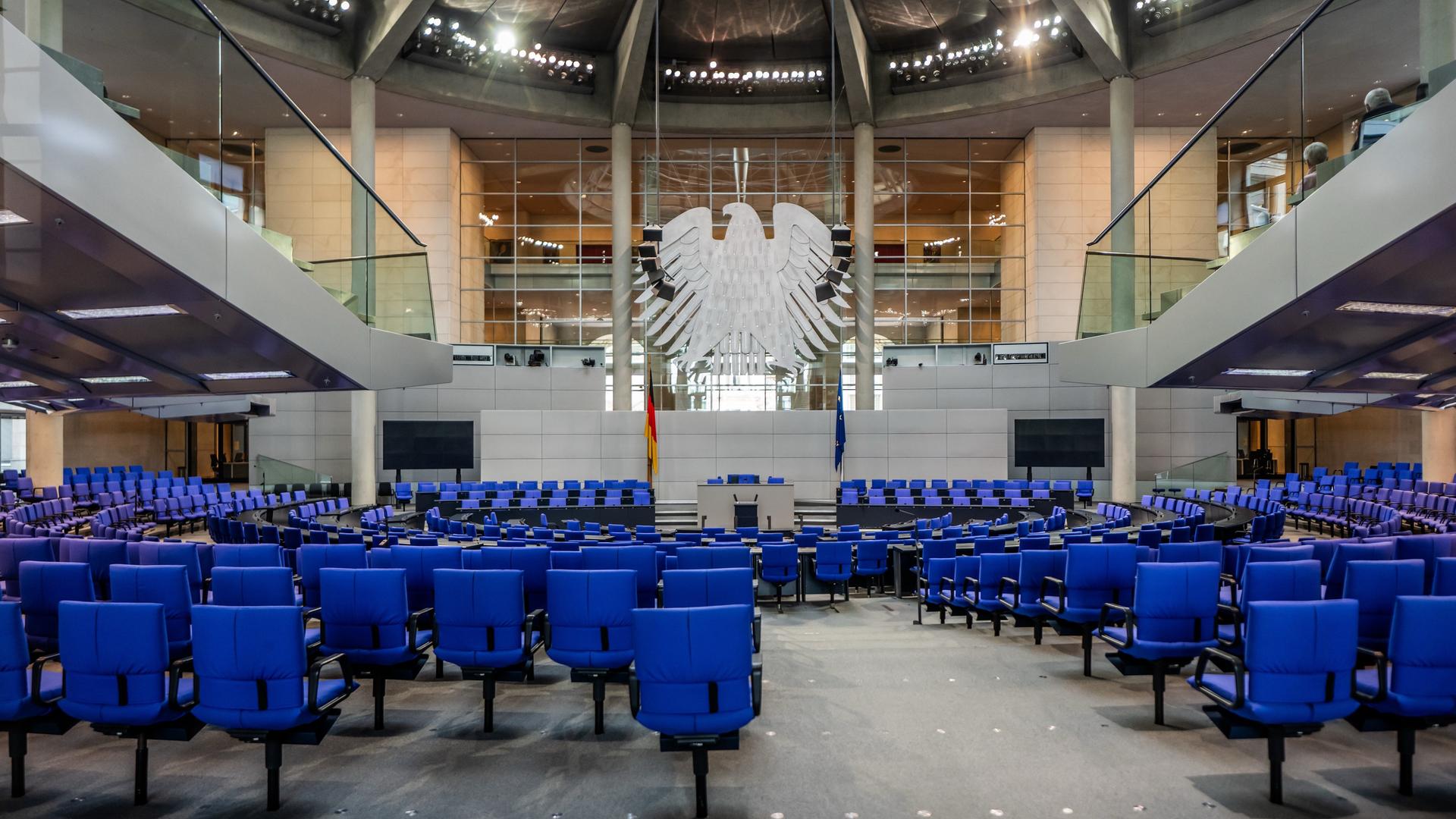 Blick in den leeren Plenarsaal im deutschen Bundestag. Vorne hängt der Bundesadler. 