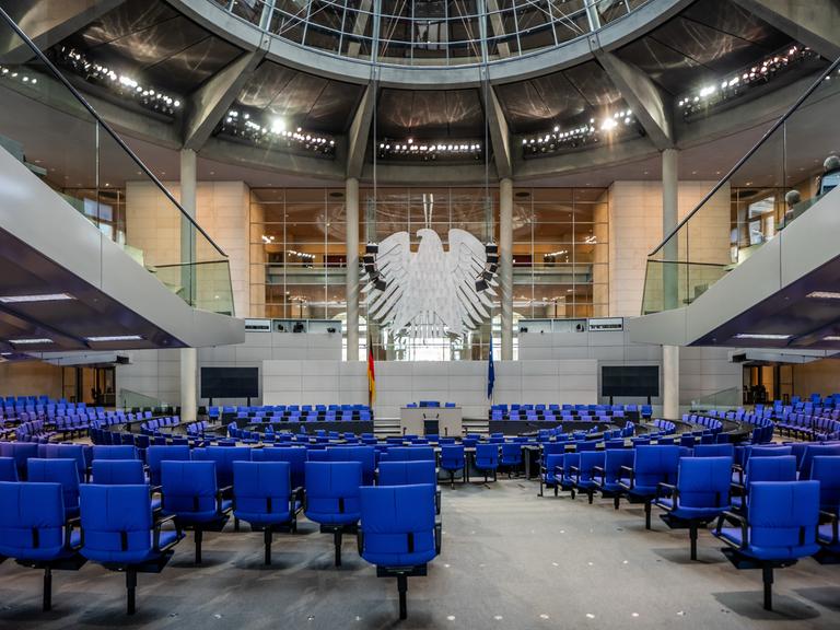 Blick in den leeren Plenarsaal im deutschen Bundestag. Vorne hängt der Bundesadler. 