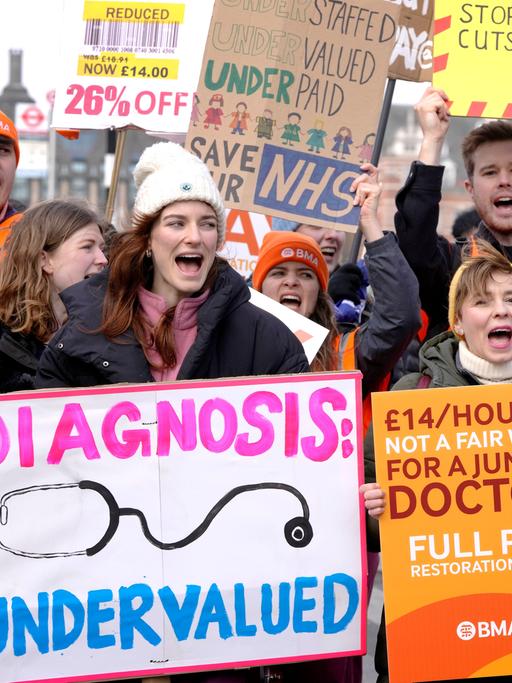 Die Männer und Frauen halten Transparente und Plakate hoch. Auf einem steht "Diagnosis Undervalued".