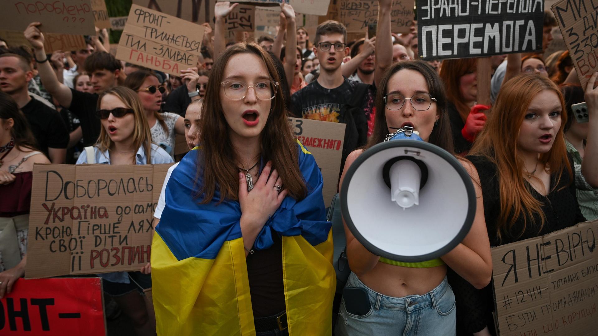 Ukrainische Demonstranten protestieren singen gegen die Pläne von Präsident Selenskyj, die Arbeit der unabhängigen Antikorruptionsbehörden einzuschränken. Eine Frau im Vordergrund hat eine ukrainische Fahne umgehängt, eine andere hält ein Megaphon. 