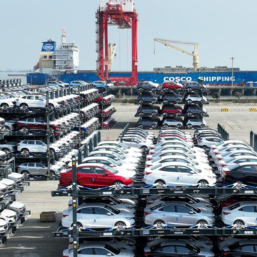 Tausende Autos stehen im Taicang Port International Container Terminal bei Schanghai in spezillen Transportrahmen. Im Hintergrund ein Schiff der Cosco-Reederei und Kräne.