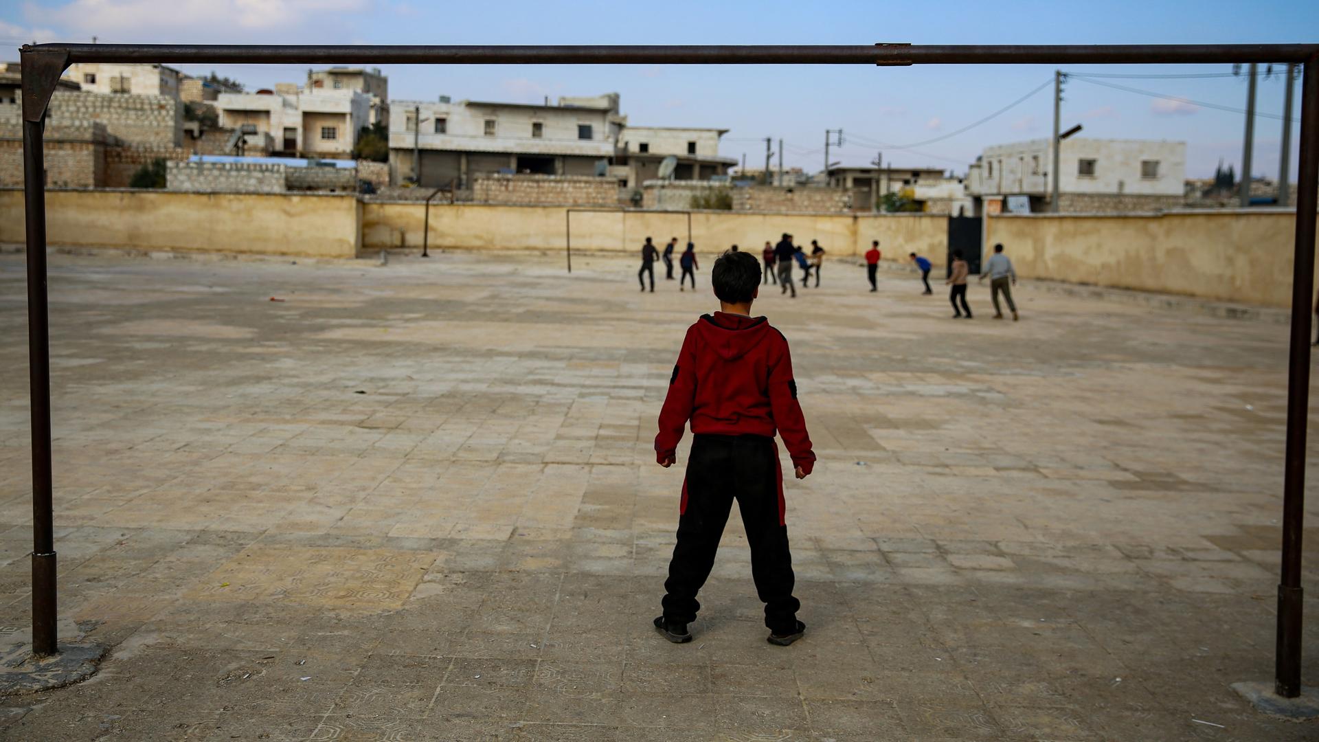 Kinder spielen auf einem Schulhof in der syrischen Stadt Taqad. Ein Junge steht mit dem Rücken vorne, weitere Kinder sind im Hintergrund. 