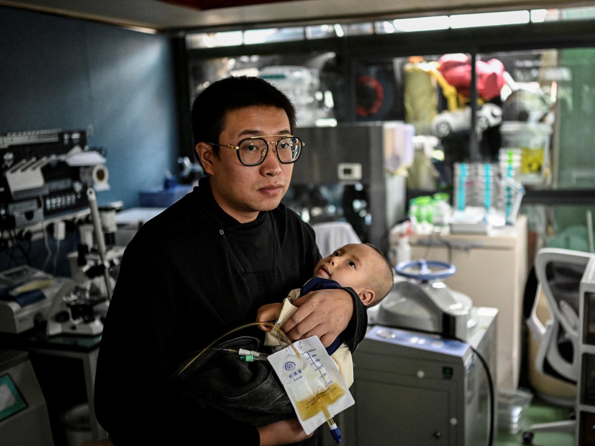 Das am 20. Oktober 2021 aufgenommene Foto zeigt Xu Wei (links), wie er seinen Sohn Xu Haoyang, bei dem das Menkes-Syndrom diagnostiziert wurde, in seinem Heimlabor in Kunming in der südwestchinesischen Provinz Yunnan im Arm hält. 