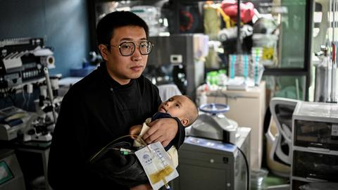 Das am 20. Oktober 2021 aufgenommene Foto zeigt Xu Wei (links), wie er seinen Sohn Xu Haoyang, bei dem das Menkes-Syndrom diagnostiziert wurde, in seinem Heimlabor in Kunming in der südwestchinesischen Provinz Yunnan im Arm hält. 