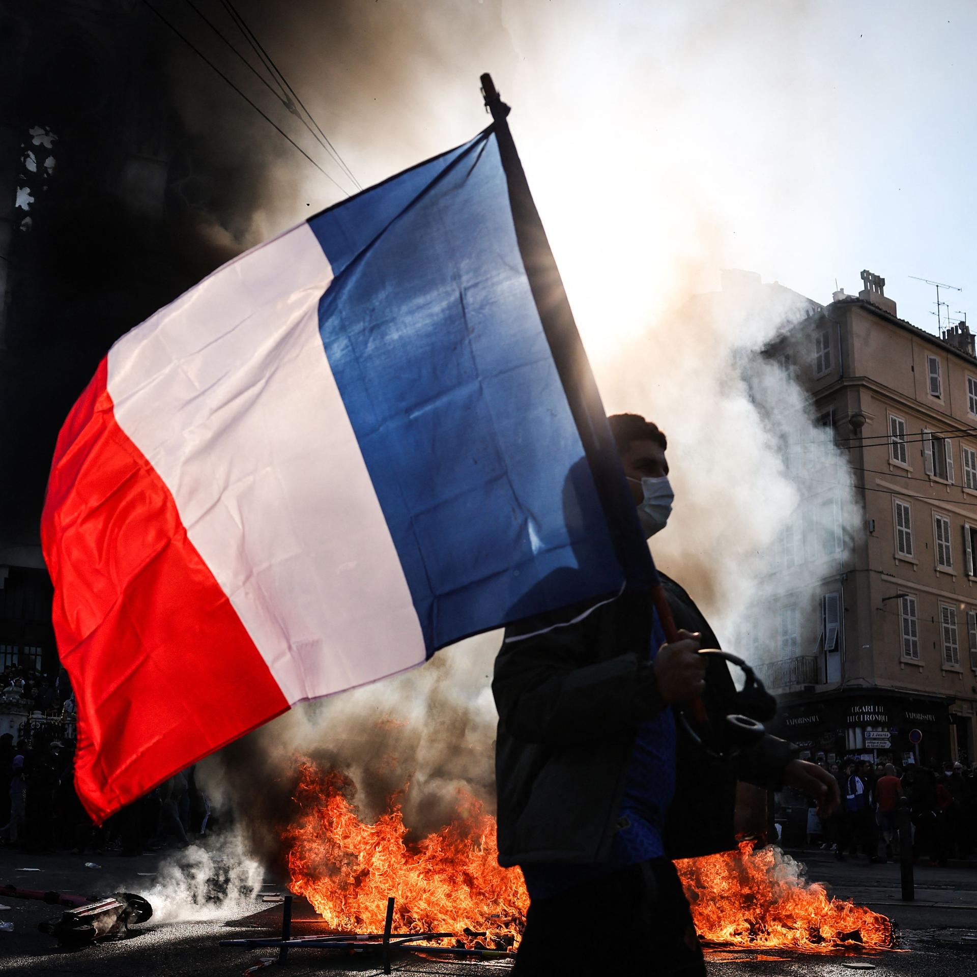 Ein Demonstrant, der eine französische Nationalflagge schwenkt, geht in Marseille an einem Feuer vorbei.