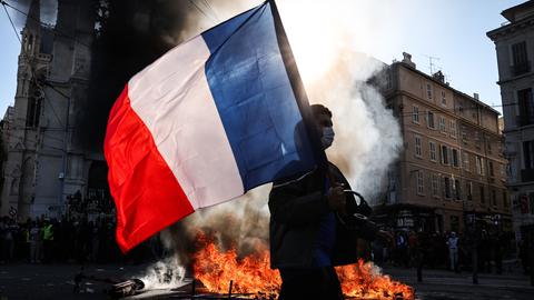 Ein Demonstrant, der eine französische Nationalflagge schwenkt, geht in Marseille an einem Feuer vorbei.
