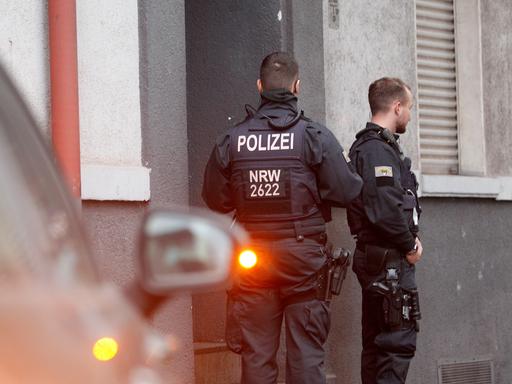 Polizisten stehen vor einem Haus.