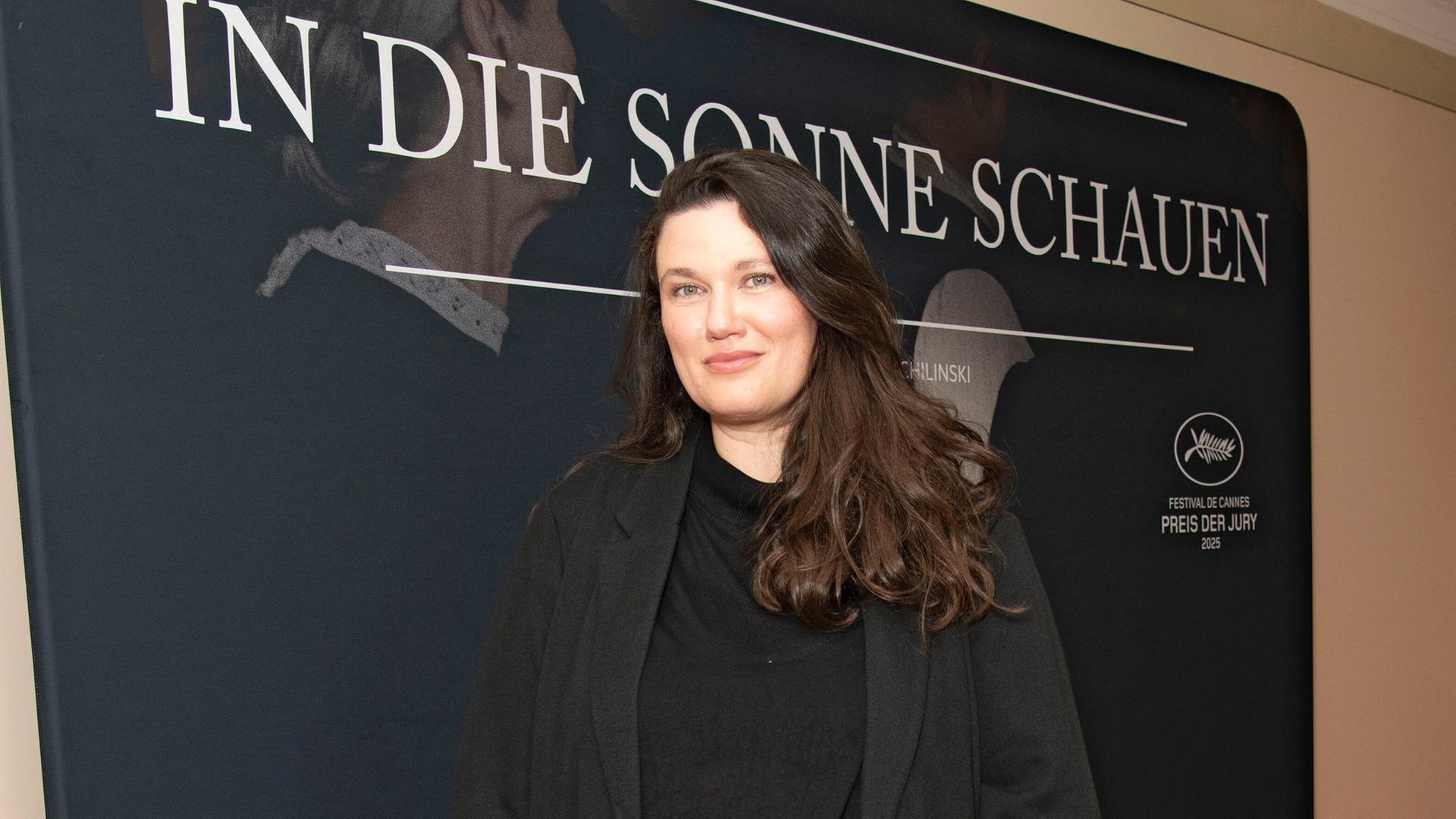 Mascha Schilinski steht auf einem roten Teppich. Hinter ihr ist ein Plakat von dem Film "In die Sonne schauen". 