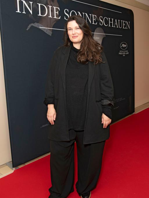 Mascha Schilinski steht auf einem roten Teppich. Hinter ihr ist ein Plakat von dem Film "In die Sonne schauen". 
