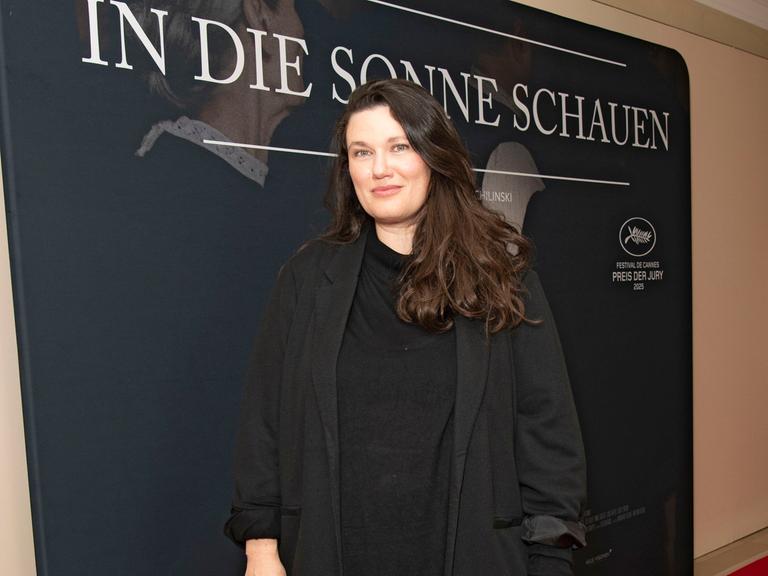 Mascha Schilinski steht auf einem roten Teppich. Hinter ihr ist ein Plakat von dem Film "In die Sonne schauen". 