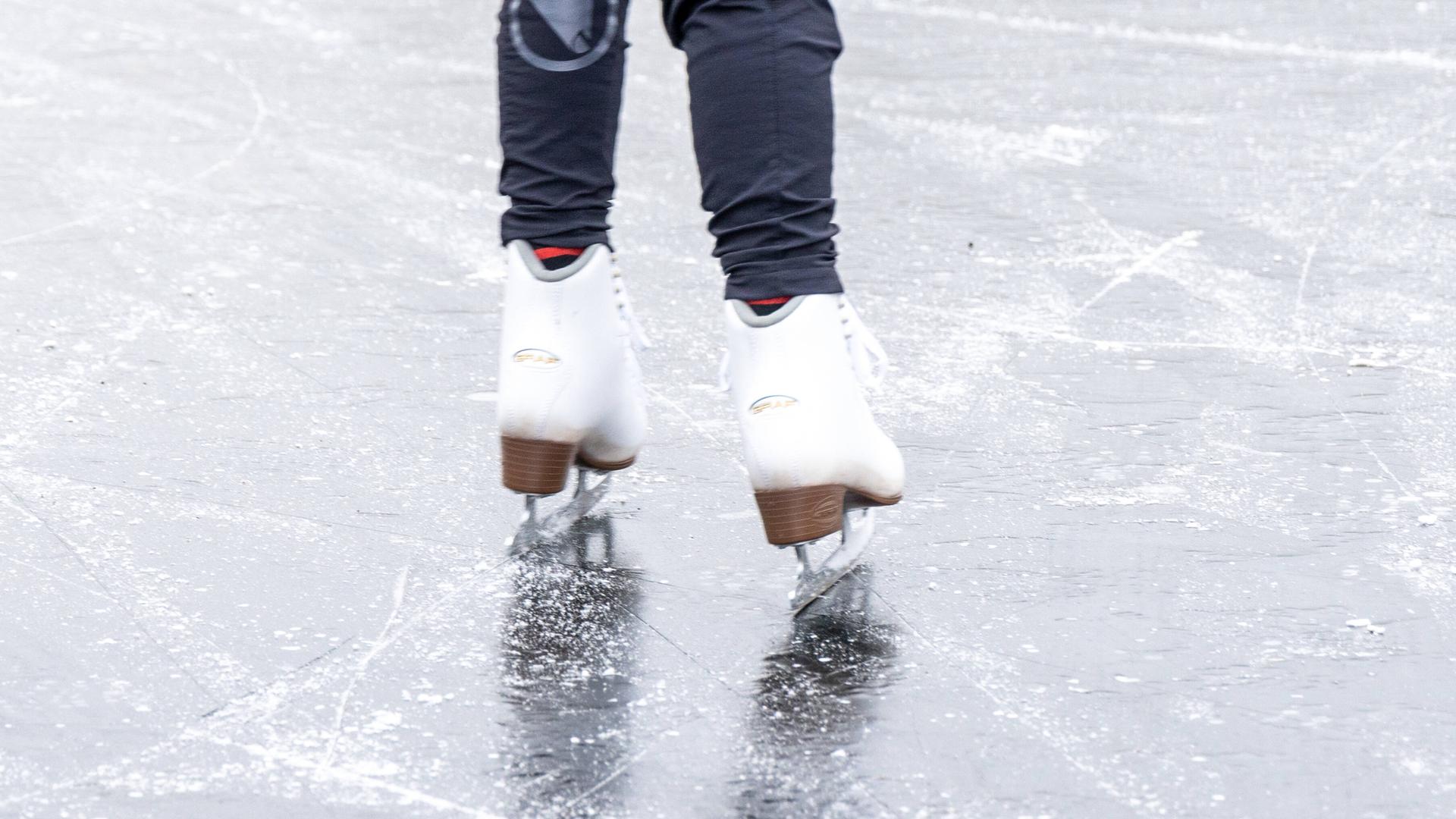Man sieht die Beine mit Schlittschuhen von einer Person auf einer Eisfläche.