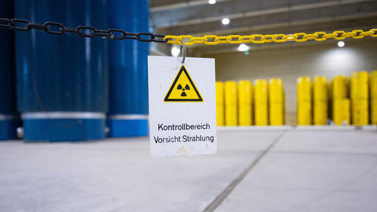 Gelbe und blaue Castor-Behälter stehen penibel gestapelt in einer großen, hellen unterirdischen Halle. Auf einem Schild im Bildvordergrund steht "Kontrollbereich - Vorsicht Strahlung"
