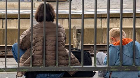 Eine Mutter sitzt mit ihrem Kind auf dem Boden eines Bahnhofs