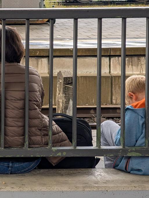 Eine Mutter sitzt mit ihrem Kind auf dem Boden eines Bahnhofs