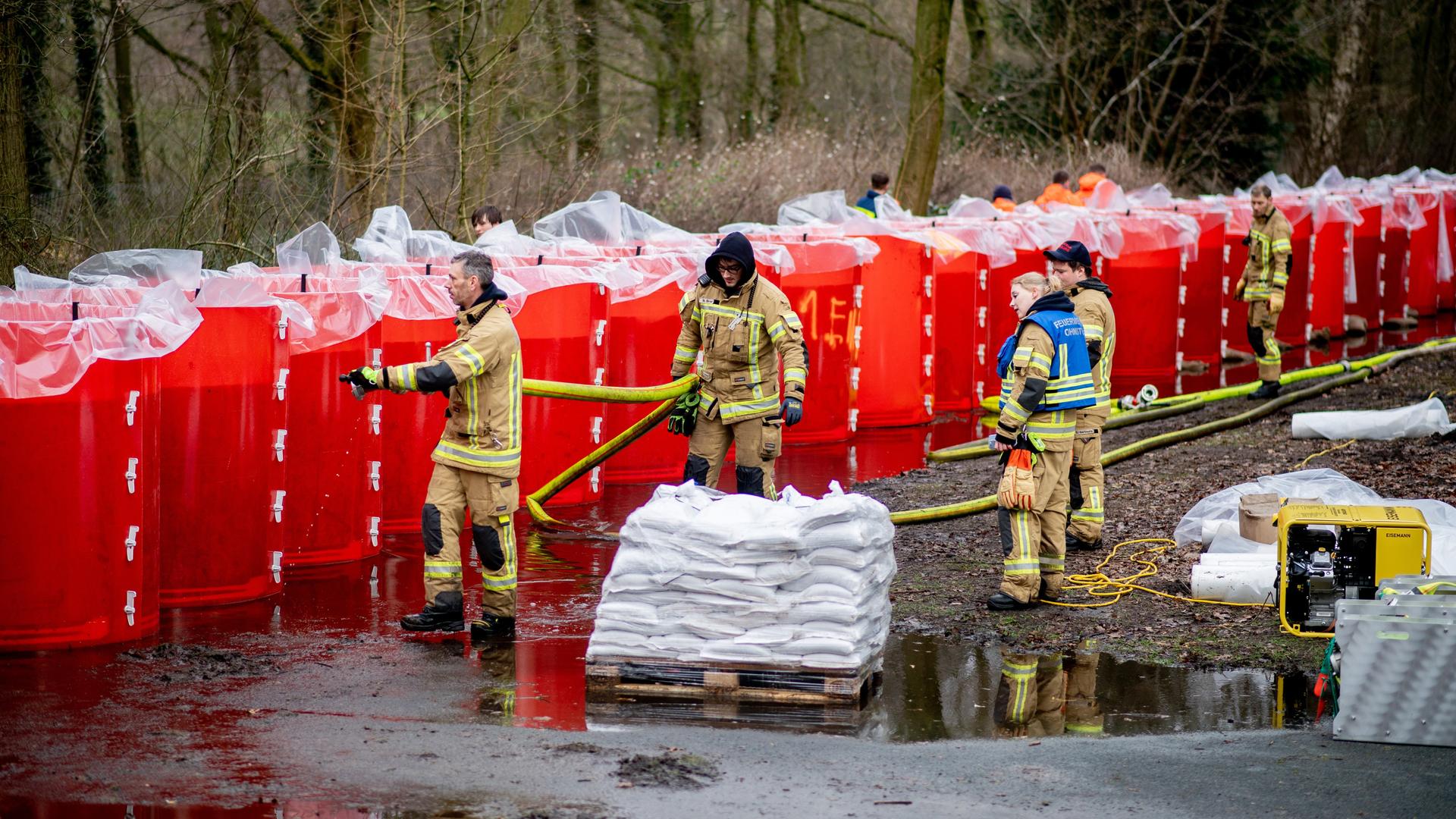 Einsatzkräfte der Feuerwehr befüllen ein mobiles Deichsystem, bestehend aus zahlreichen großen Behältern mit Wasser.