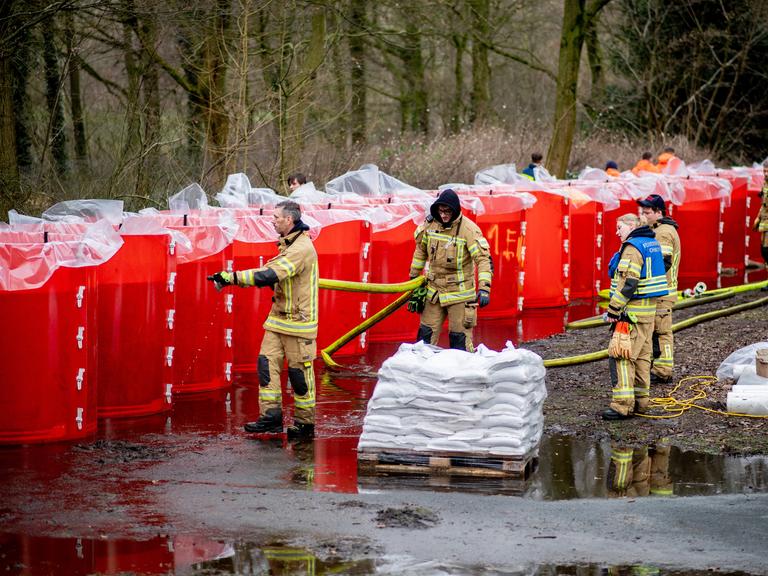 Einsatzkräfte der Feuerwehr befüllen ein mobiles Deichsystem, bestehend aus zahlreichen großen Behältern mit Wasser.