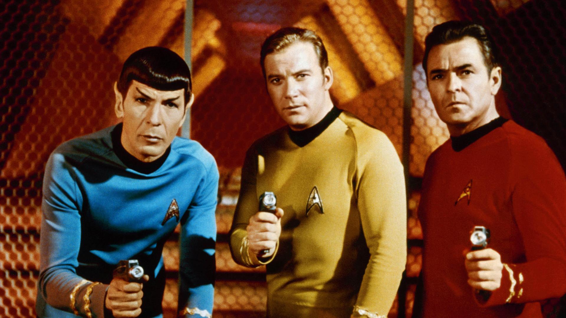 Mr. Spock, Captain James T. Kirk und Scotty (Leonard Nimoy, William Shatner, James Doohan) tragen ihre Raumschiffanzüge aus der Fernsehserie "Star Trek" und halten Waffen in den Händen.