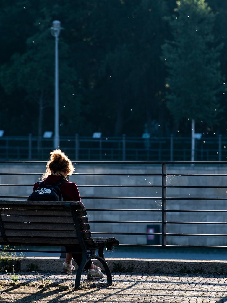 Eine Frau sitzt am Morgen allein auf einer Bank im Berliner Regierungsviertel. Sie trägt einen Rücksack. Vor ihr ist ein Fluß.