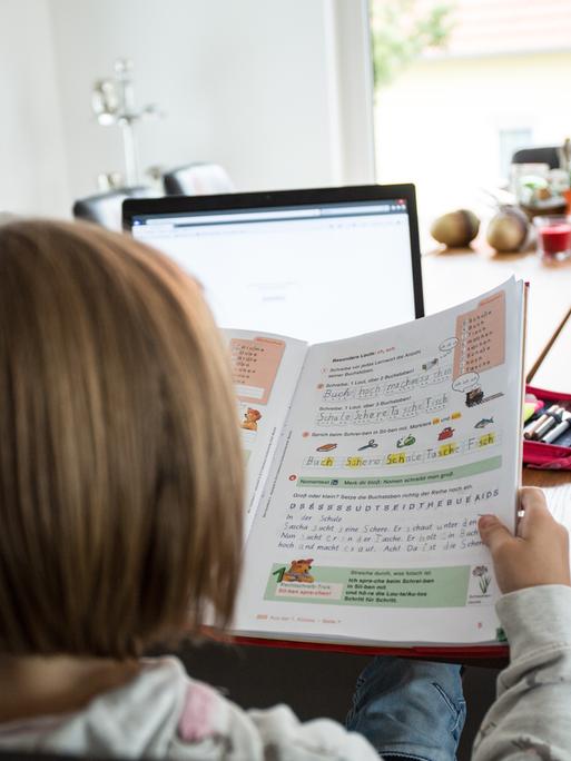 Ein junges Mädchen sitzt am Wohnzimmertisch an einem Laptop und macht Homeschooling zu Hause.