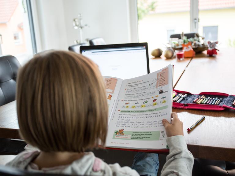 Ein junges Mädchen sitzt am Wohnzimmertisch an einem Laptop und macht Homeschooling zu Hause.
