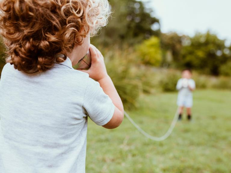 Ein Junge spricht in ein Dosentelefon.
