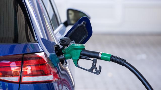 Eine Zapfpistole für Benzin steckt in einer Tankstelle im Tankstutzen eines Autos. 