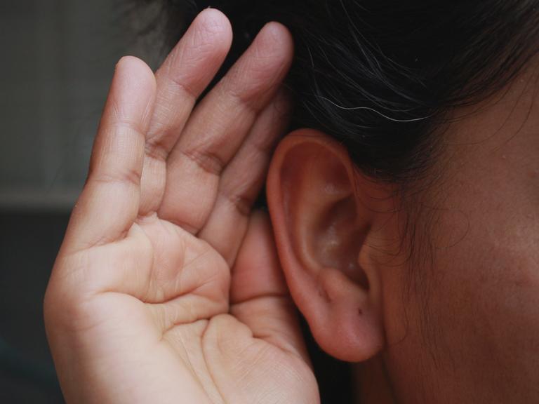 Wie können wir uns beim Hören selbst zuhören? Zu sehen: Eine Hand ist geöffnet an einem Ohr. 