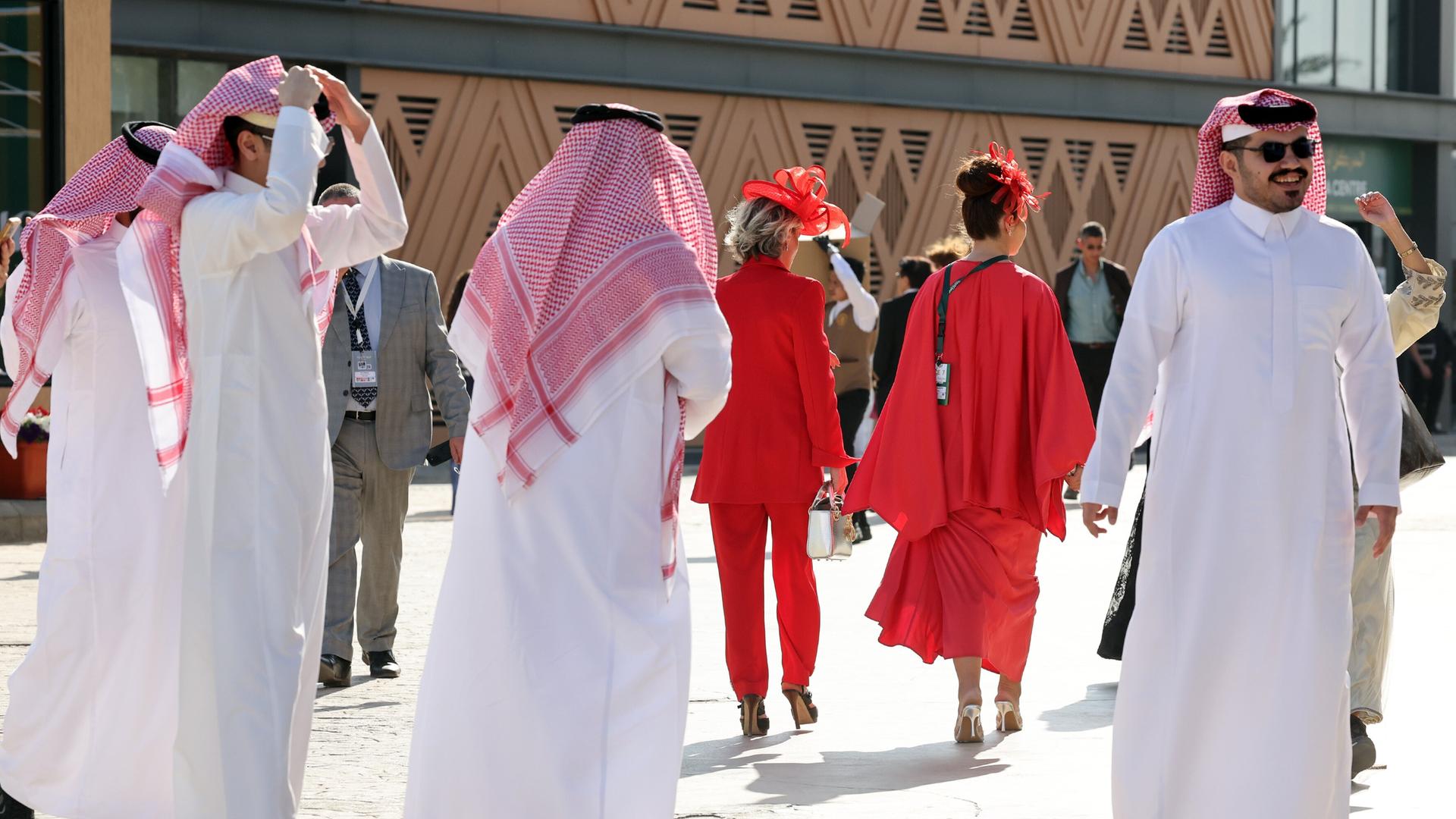 Männer in saudischer Landestracht neben westlich gekleideten Frauen ganz in rot Männer in saudischer Landestracht neben westlich gekleideten Frauen ganz in rot