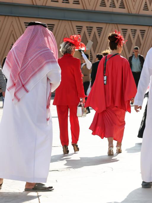 Männer in saudischer Landestracht neben westlich gekleideten Frauen ganz in rot