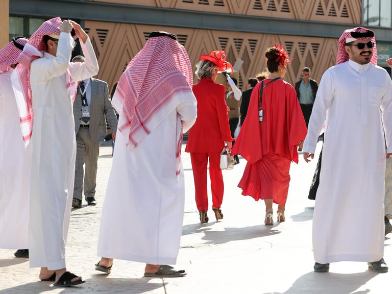 Männer in saudischer Landestracht neben westlich gekleideten Frauen ganz in rot