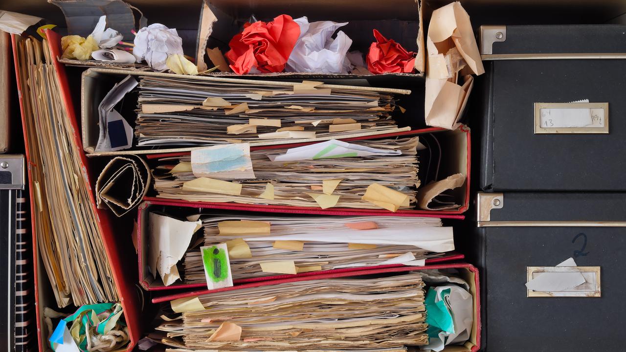 Ein Regal voll von unordentlichen Aktenordnern, alten Papieren, zerknüllten Papierkugeln und Kisten.