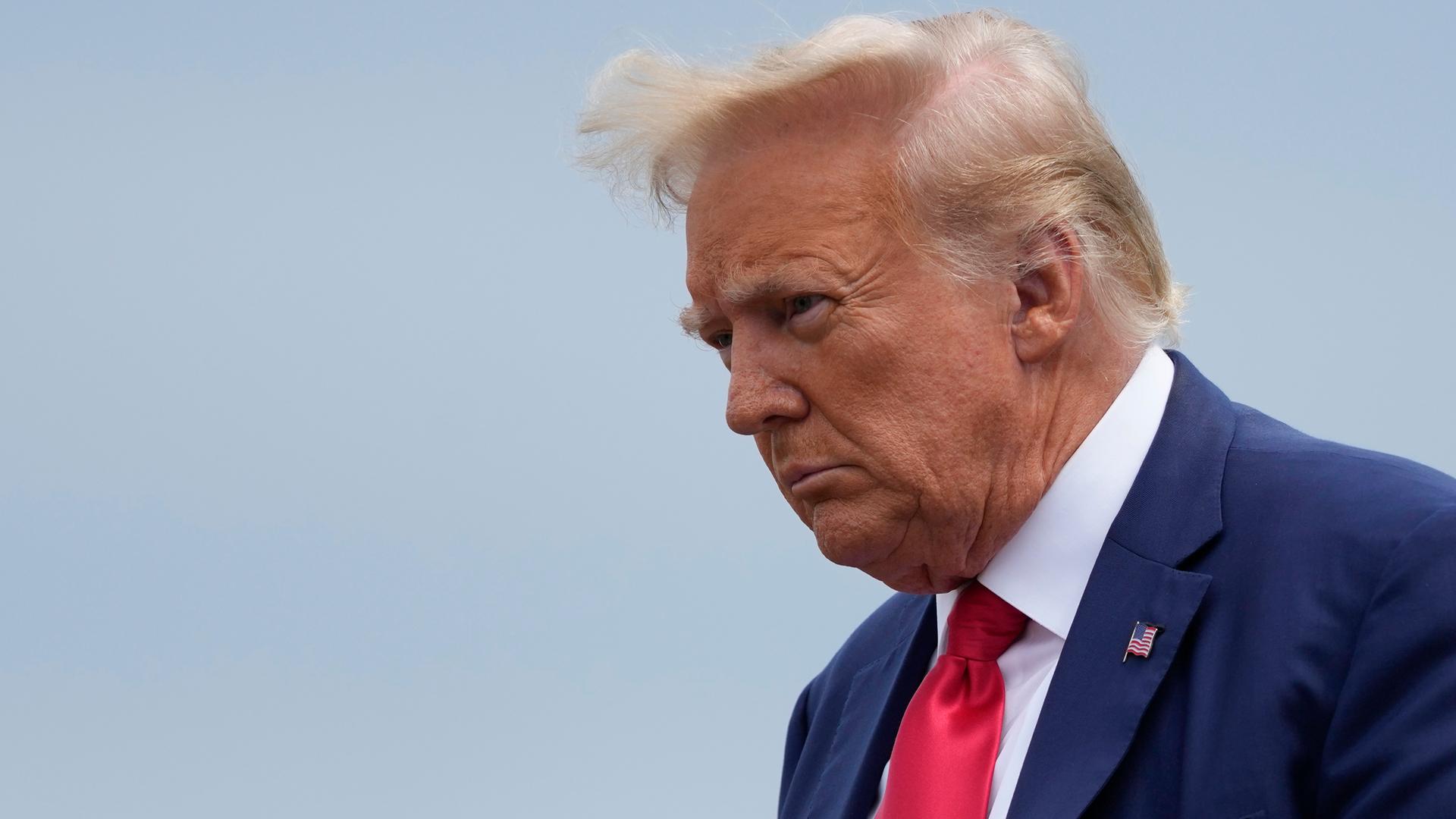 Eine Nahaufnahme von Donald Trumps Gesicht vor graublauem Himmel.
