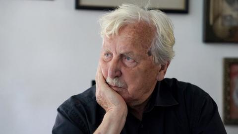 Der Autor Arno Surminski sitzt an einem Tisch in seiner Wohnung und schaut zur Seite. 