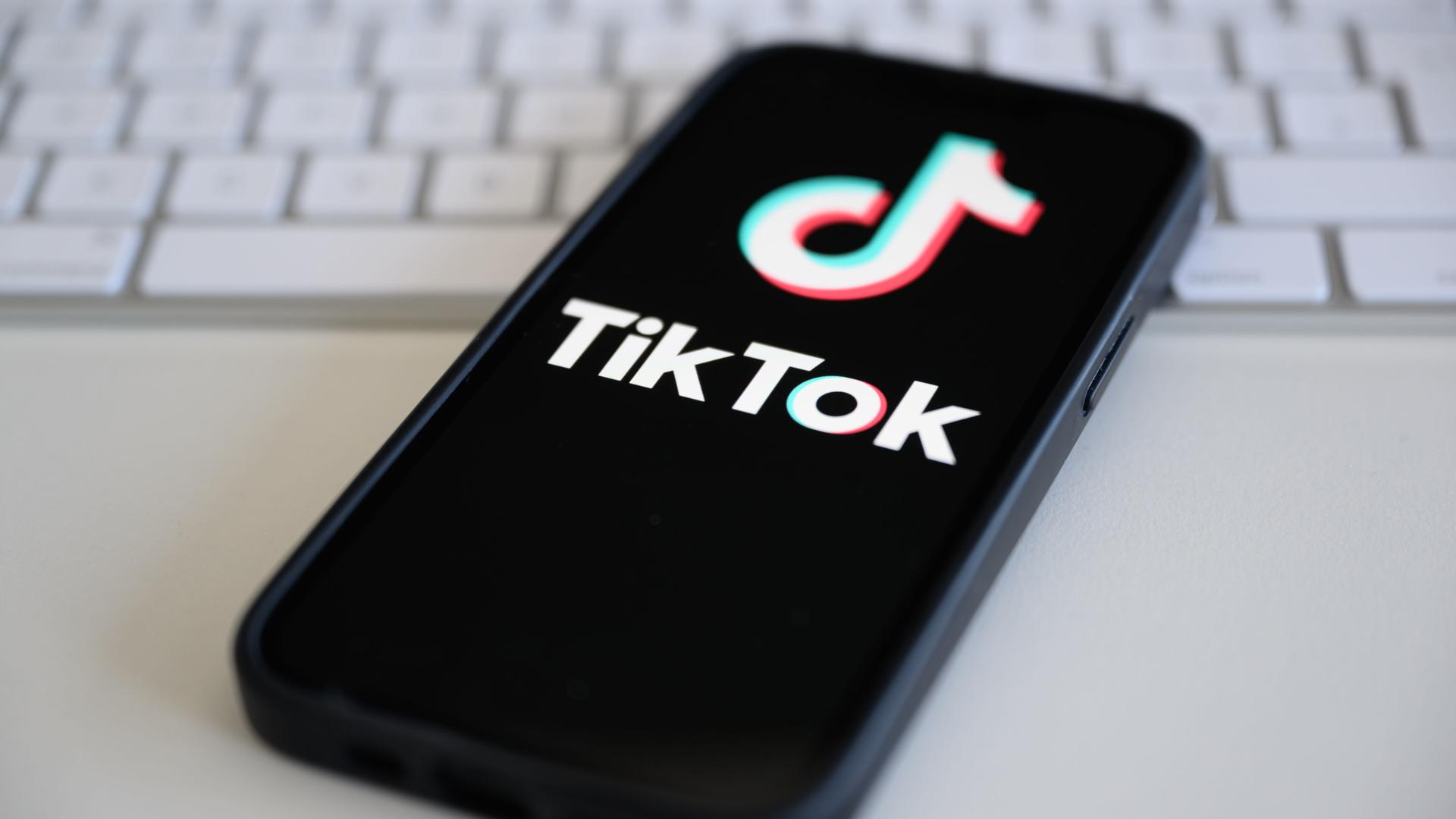 Auf einem Smartphone, das auf einer Computertstatur liegt, wird das Logo von TikTok angezeigt.