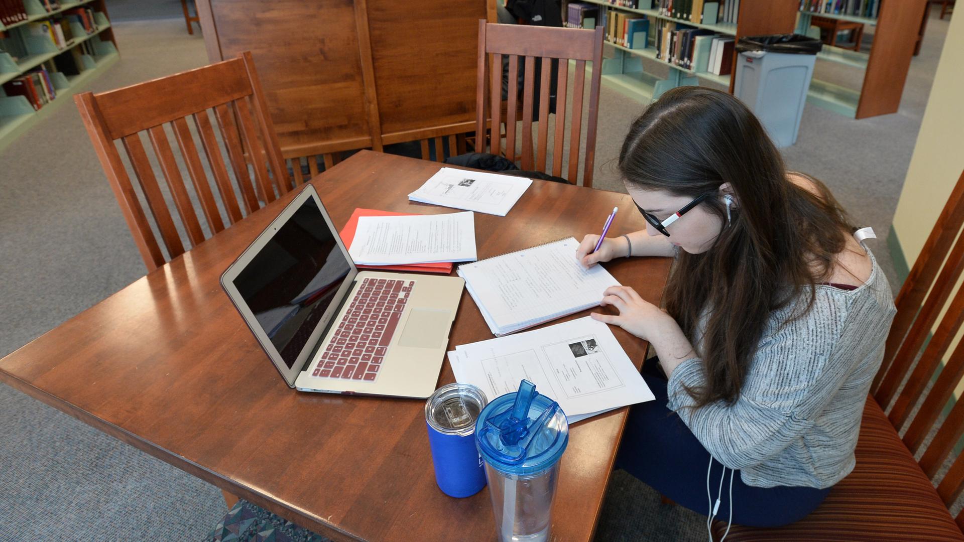 Eine Studentin in den USA sitzt in einer Bibliothek an einem Tisch und arbeitet. Eine Studentin in den USA sitzt in einer Bibliothek an einem Tisch und arbeitet.