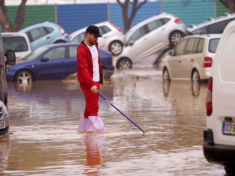 Ein Mann läuft durch das überflutete Valencia. Im Hintergrund Autos, die teilweise übereinander stehen.