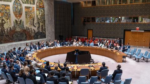In einem Saal ohne Fenster sitzen Vertreter der Mitglieder des UNO-Sicherheitsrats an einem runden Tisch. An der Rückwand ist ein deckenhohes Gemälde.