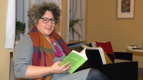 Autorin und Abenteurerin Rebecca Maria Salentin sitzt mit einem Buch auf einem Stuhl und schaut seitwärts in die Kamera.