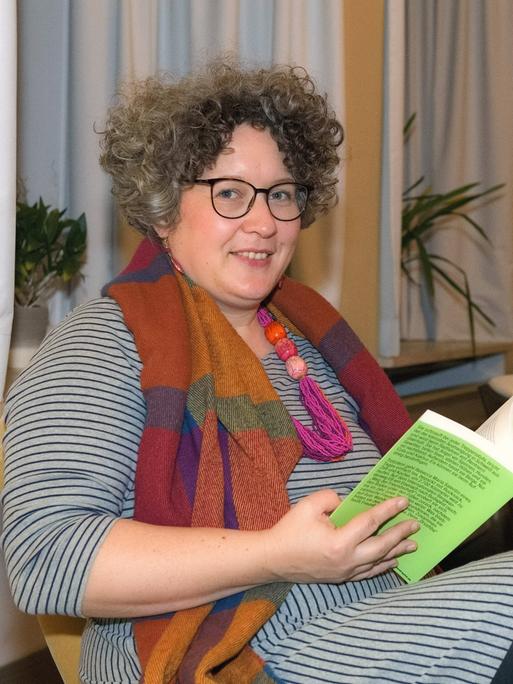 Autorin und Abenteurerin Rebecca Maria Salentin sitzt mit einem Buch auf einem Stuhl und schaut seitwärts in die Kamera.