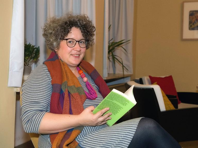 Autorin und Abenteurerin Rebecca Maria Salentin sitzt mit einem Buch auf einem Stuhl und schaut seitwärts in die Kamera.