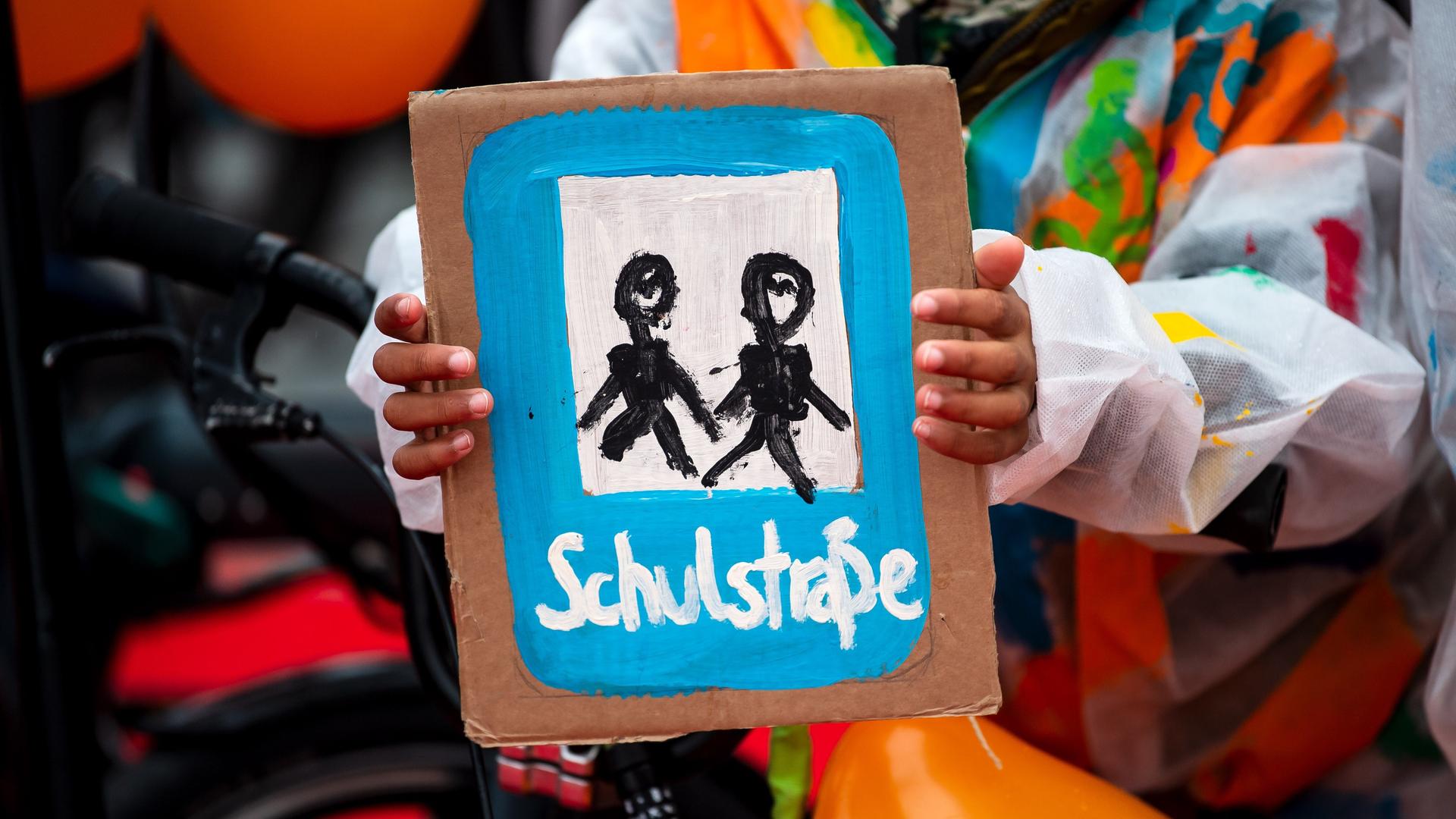 Ein Kind hält ein selbstgemaltes Plakat mit der Aufschrift "Schulstraße". Ein Bündnis lokaler und überregionaler Organisationen demonstriert vor dem Veranstaltungsort der Verkehrsministerkonferenz im Jahr 2022.