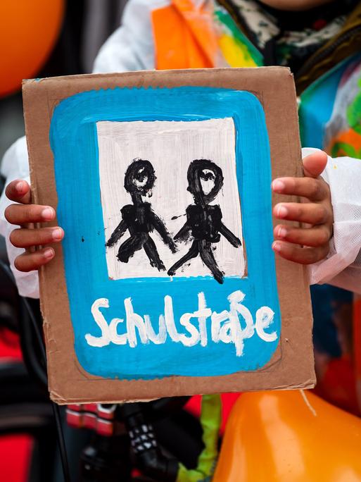 Ein Kind hält ein selbstgemaltes Plakat mit der Aufschrift "Schulstraße". Ein Bündnis lokaler und überregionaler Organisationen demonstriert vor dem Veranstaltungsort der Verkehrsministerkonferenz im Jahr 2022.