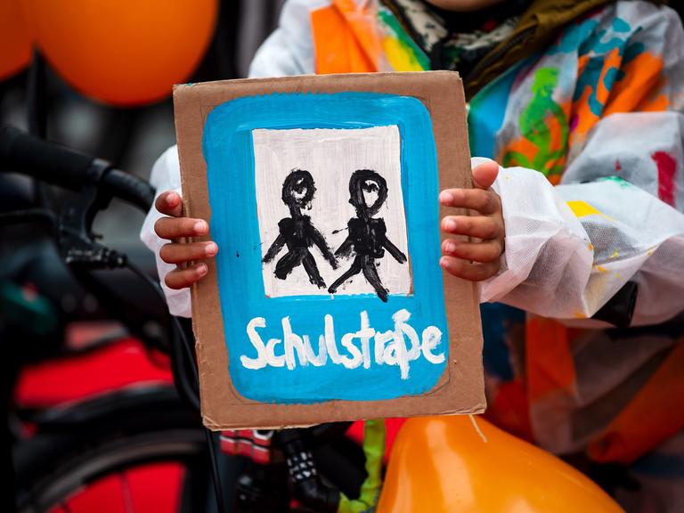 Ein Kind hält ein selbstgemaltes Plakat mit der Aufschrift "Schulstraße". Ein Bündnis lokaler und überregionaler Organisationen demonstriert vor dem Veranstaltungsort der Verkehrsministerkonferenz im Jahr 2022.